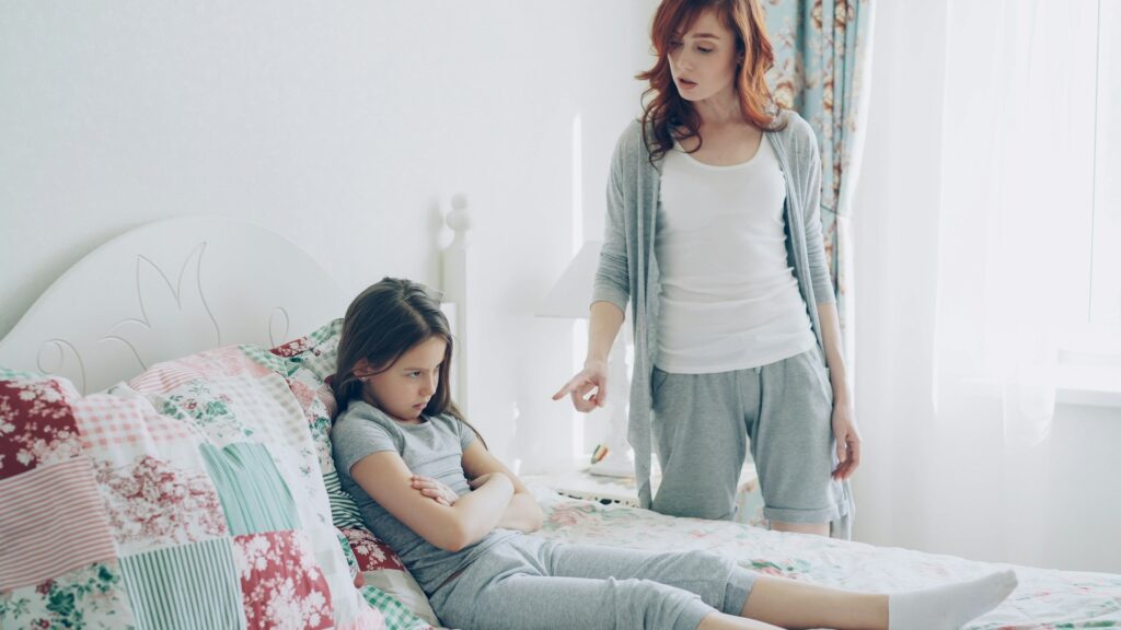 Mother scolds her daughter, who is sitting on the bed.
