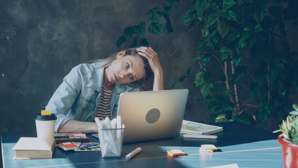 A woman appears stressed while working on laptop.
