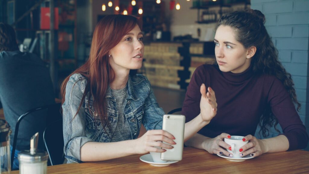 Two women converse at a cafe.
