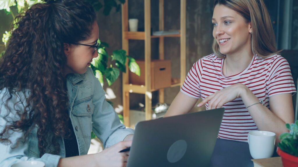 Two women work together on a laptop.
