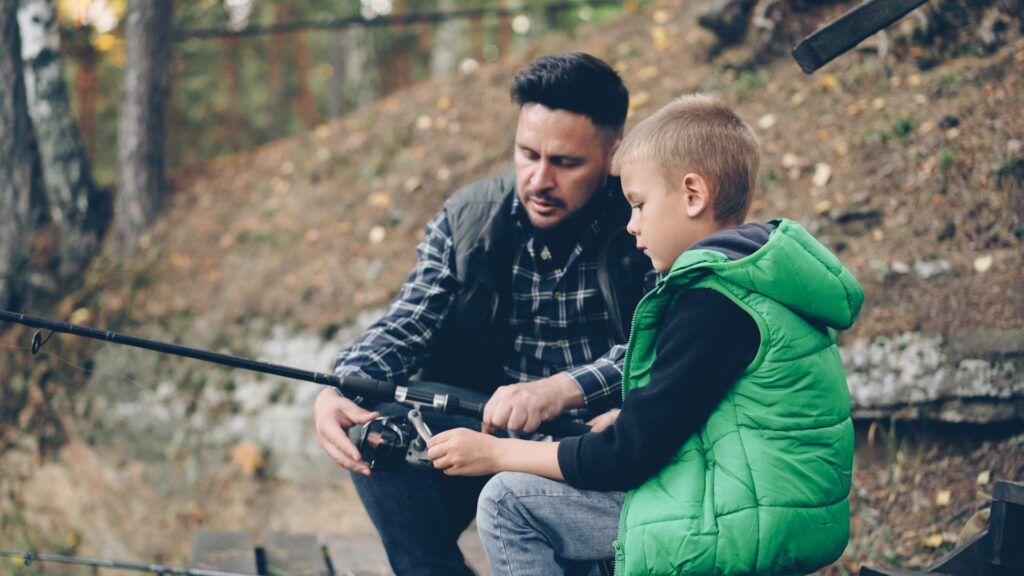 A father shows his son how to fish.
