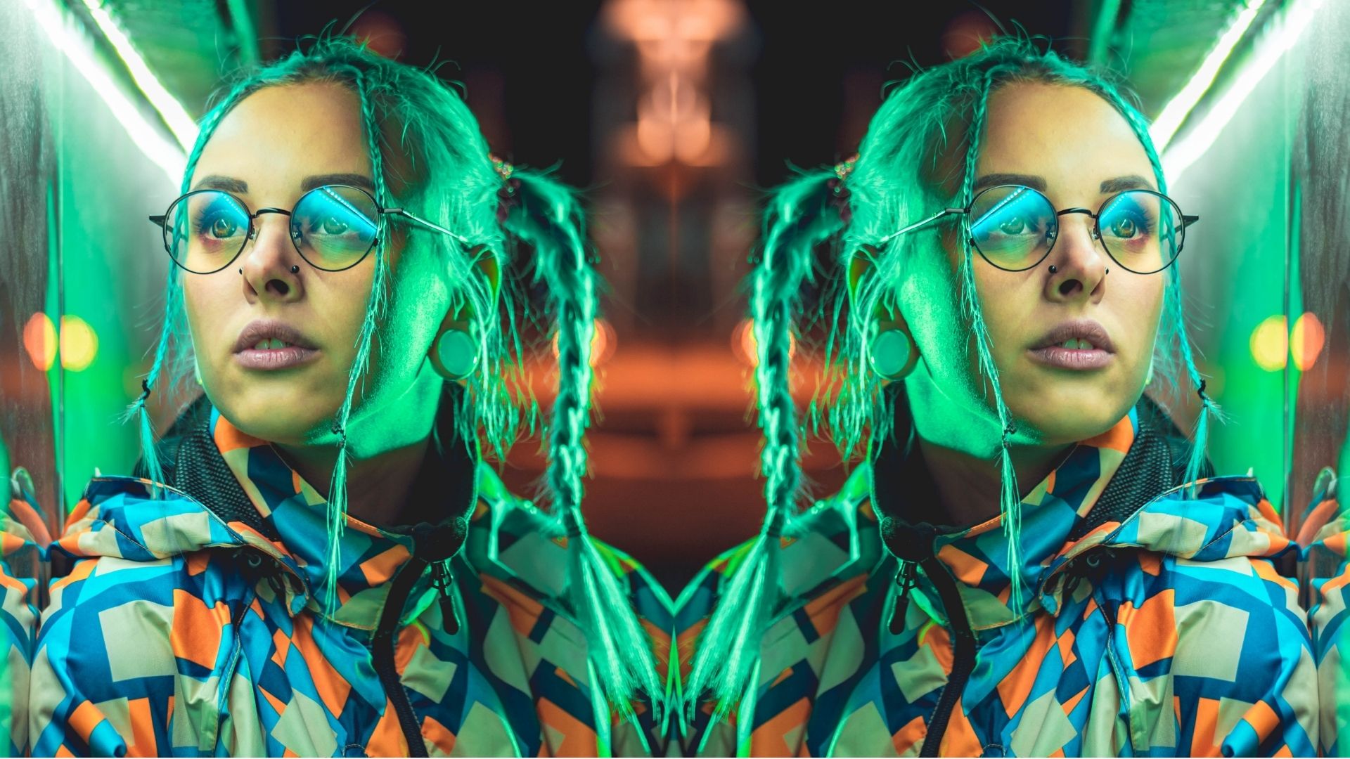 Young pretty girl with unusual hairstyle near glowing green neon light of the city at night. Dyed blue hair in braids. Pensive hipster teenager in glasses.