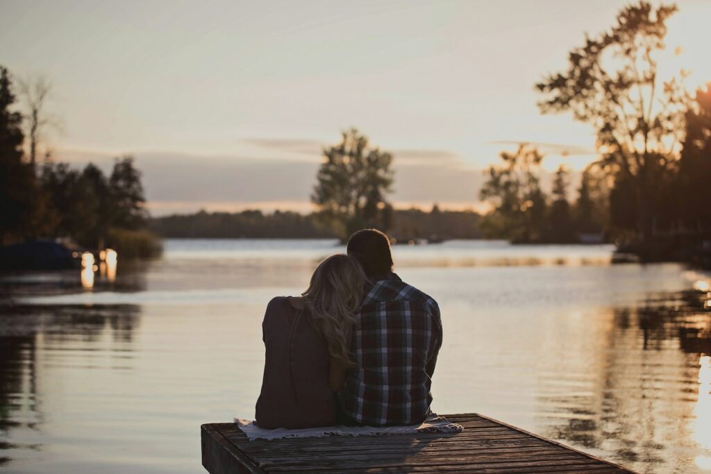 man and woman sitting on dock during golden hour
