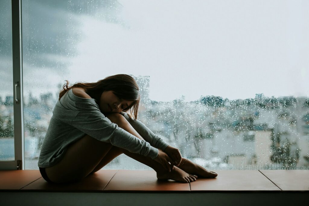 woman in gray long sleeve shirt sitting on window
