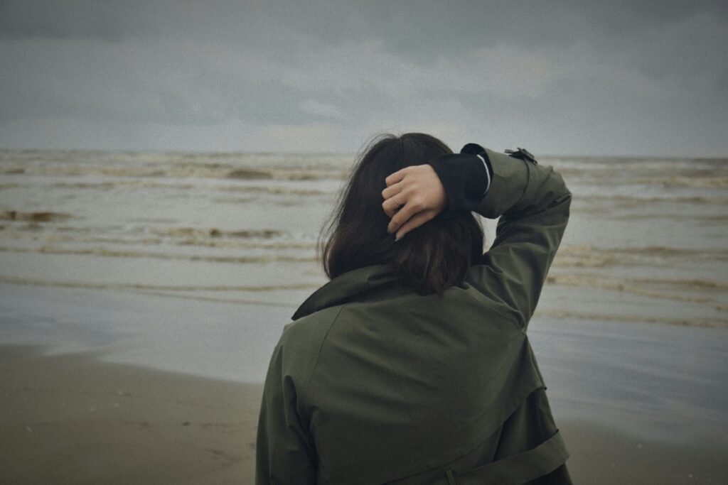 A woman standing on a beach looking at the ocean