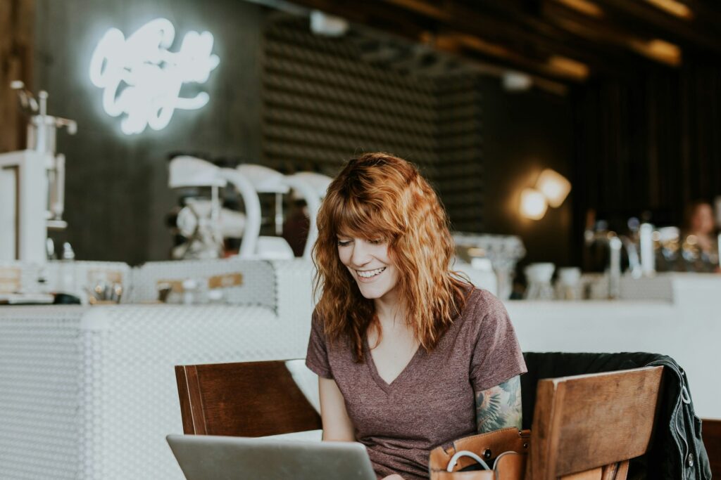 woman sitting on brown wooden chair while using silver laptop computer in room
