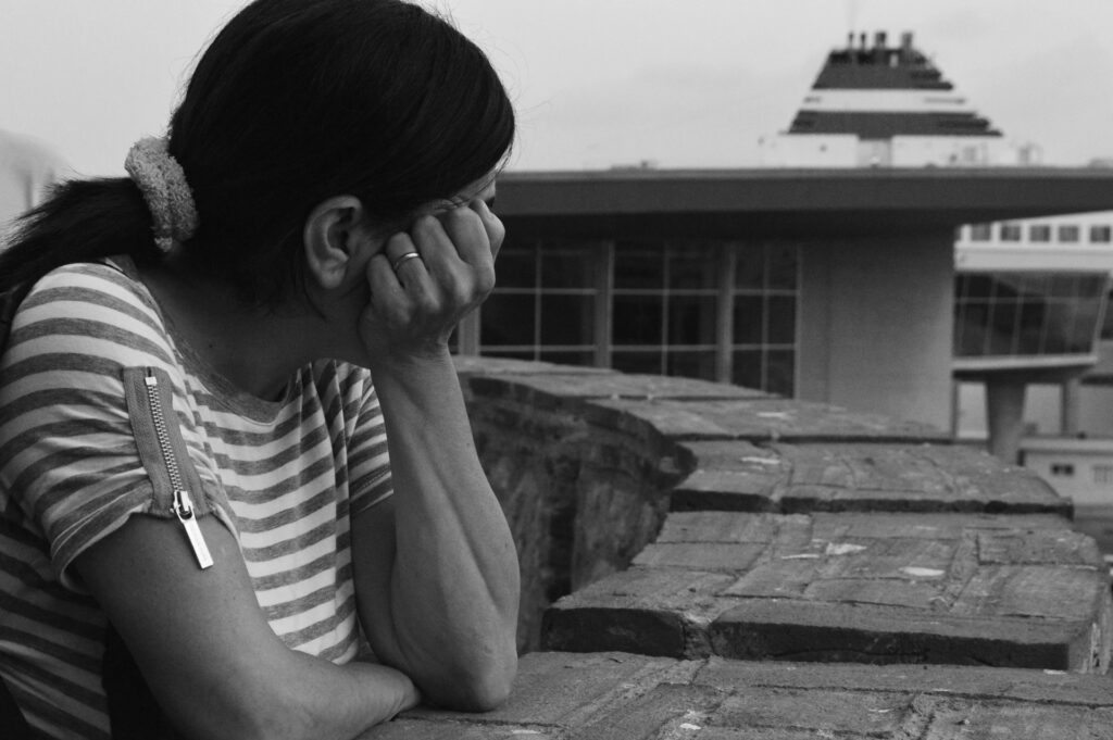 grayscale photo of woman in stripe shirt sitting on concrete bench
