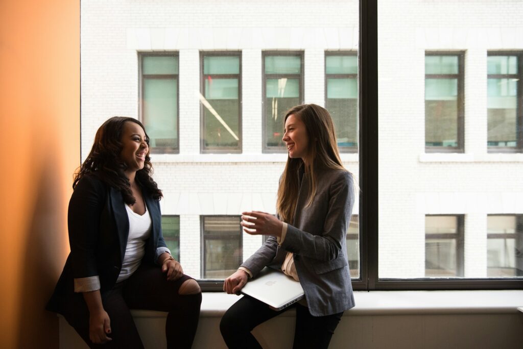 two woman sitting by the window laughing
