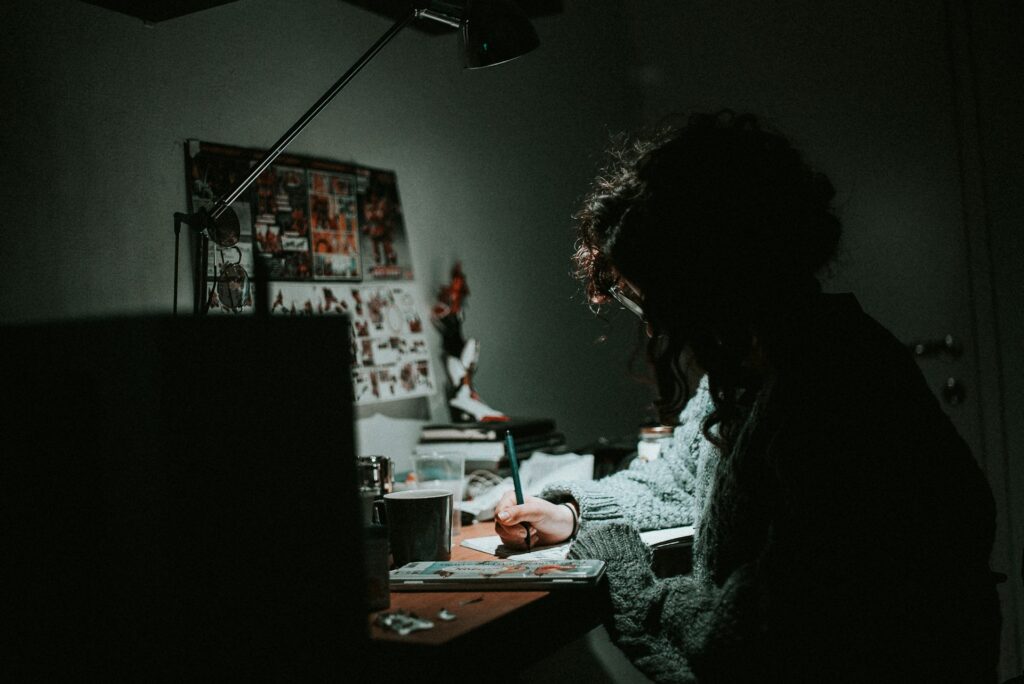low light photography of woman in gray knit sweatshirt writing on desk
