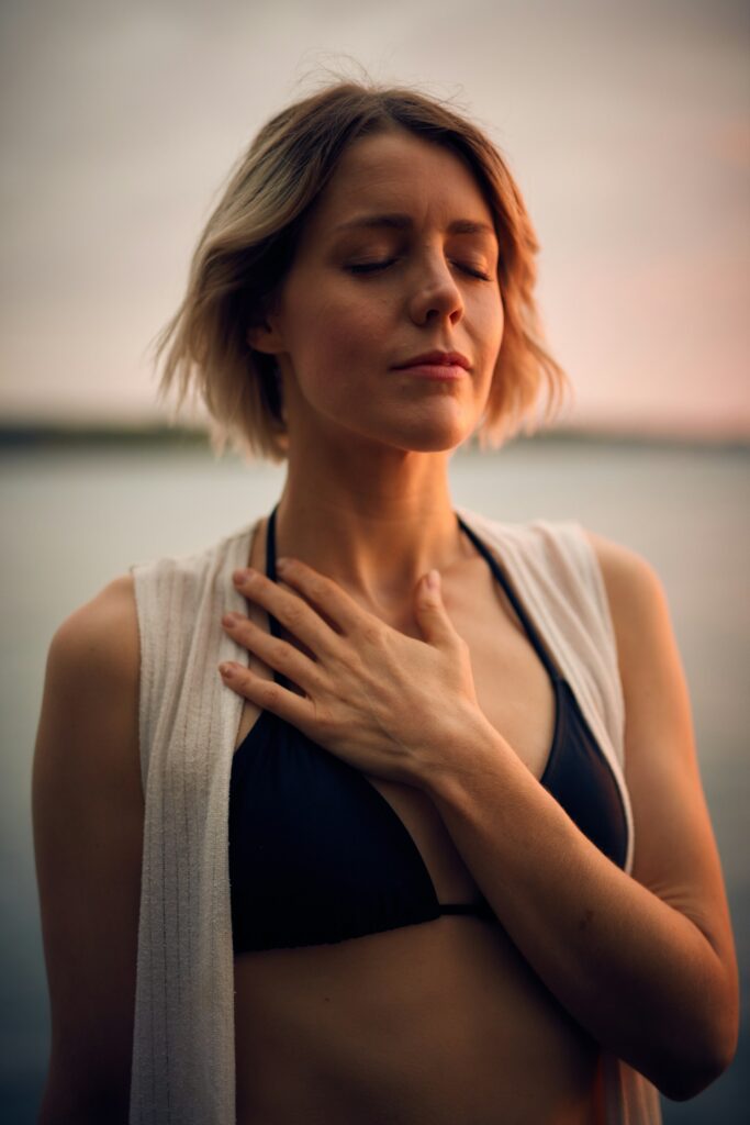 woman in white vest and black bikini with hand on chest
