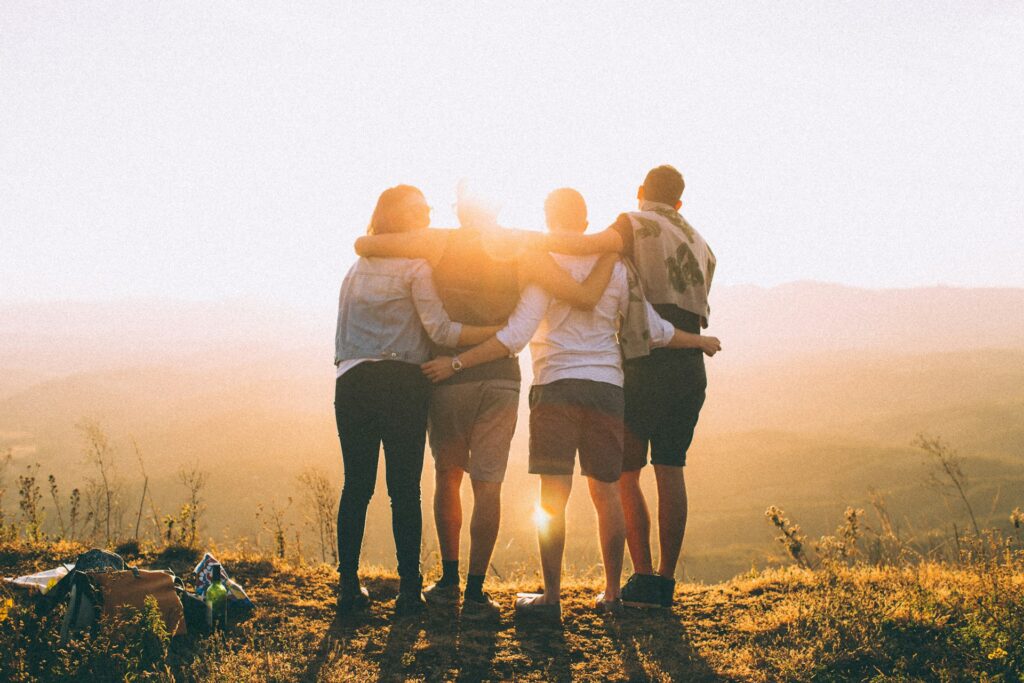 four person hands wrap around shoulders while looking at sunset
