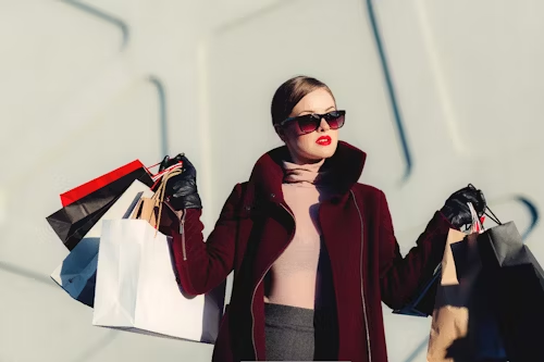Woman waring glasses and red lipstick, holding mulitiple shopping bags.