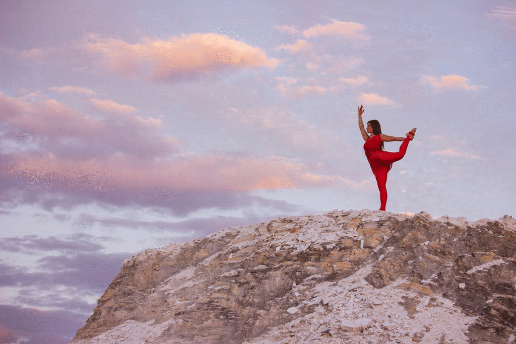 Woman in Red Practicing Yoga on Rocky Cliff at Sunset