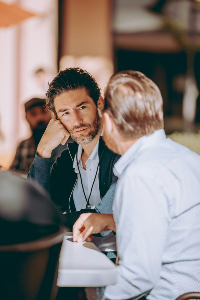 two men sitting at a table talking to each other
