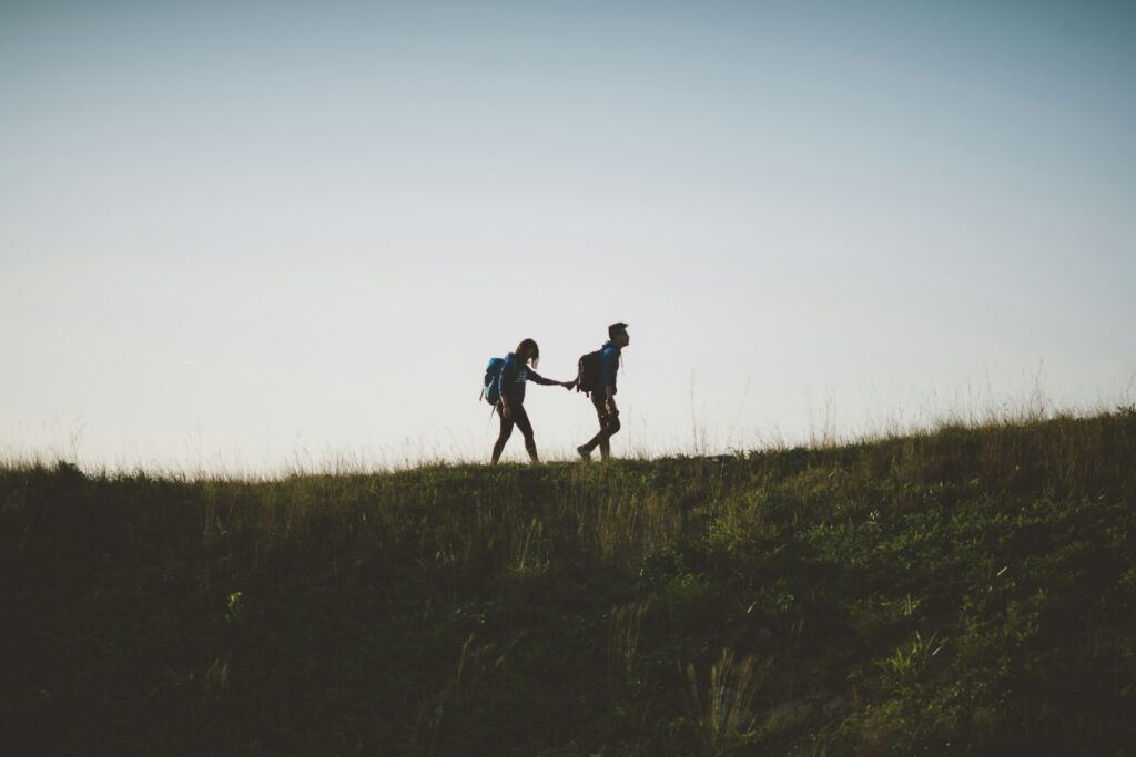 couple walking on hill while holding during daytime
