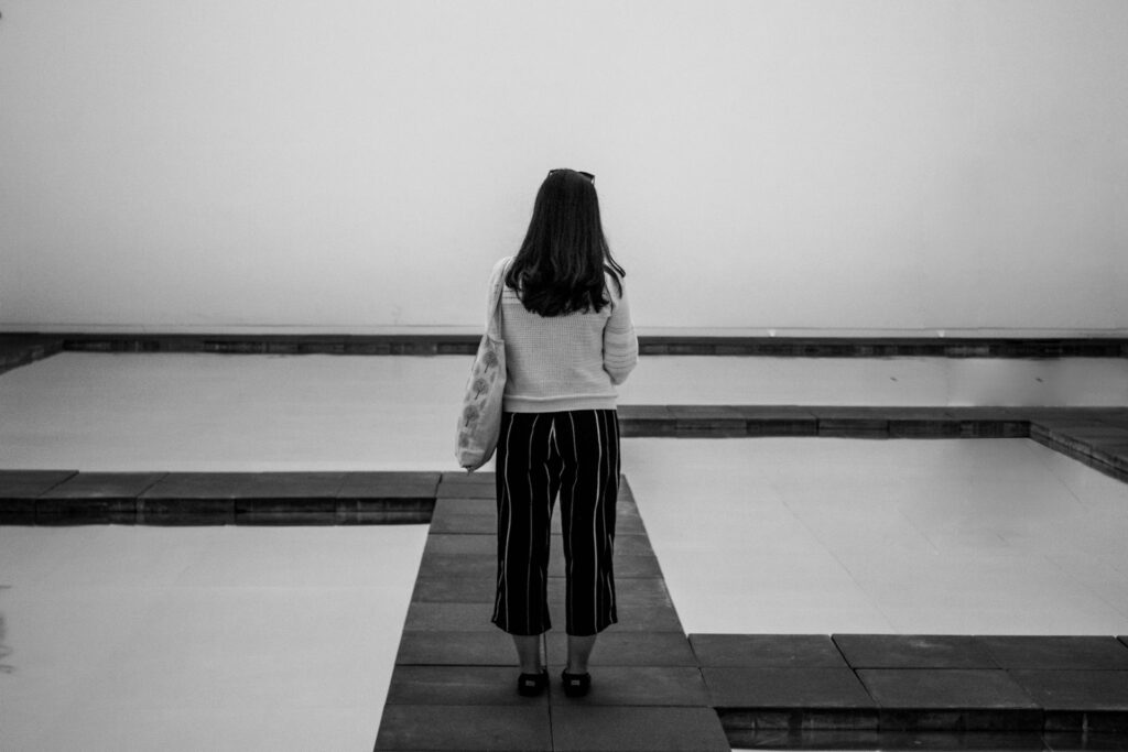 grayscale photography of woman standing beside body of water
