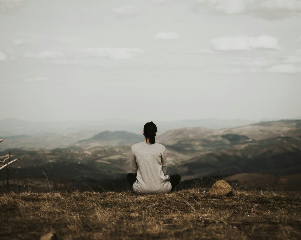 woman sitting on cliff overlooking mountains during daytime
