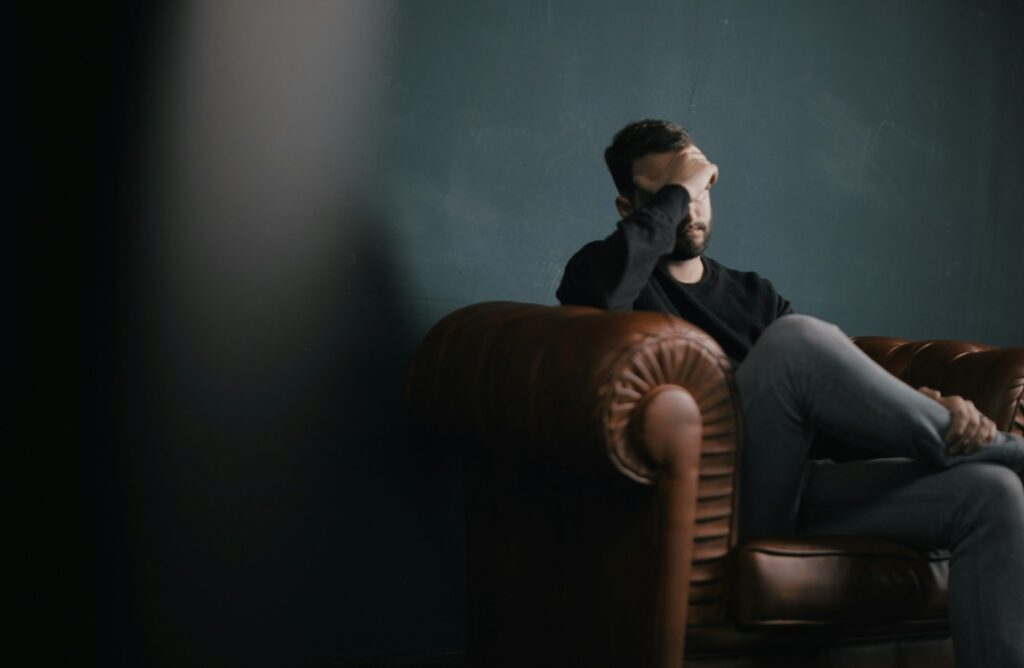 a man holds his head while sitting on a sofa
