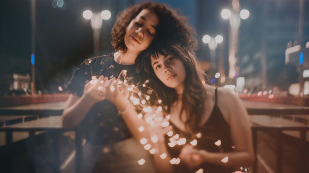 Selective Focus Photography of Two Women Holding String Lights Turned on
