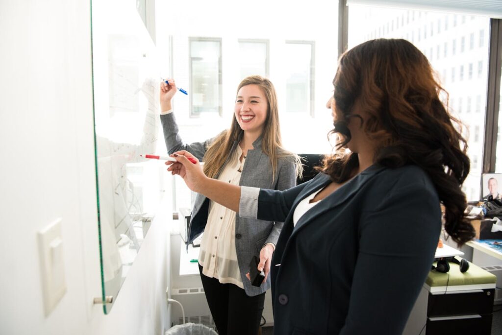 Two Women in Front of Dry-erase Board
