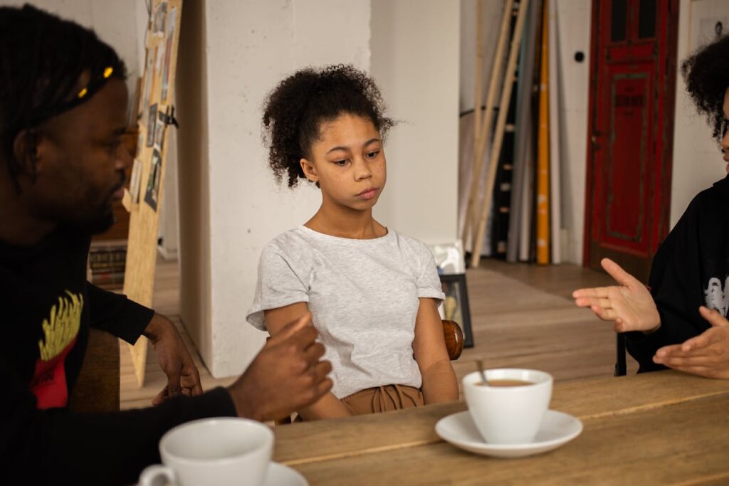 Unpleasant black girl sitting at table between parents
