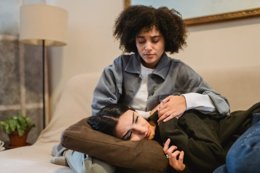 Young black woman cuddling crying female friend lying on sofa
