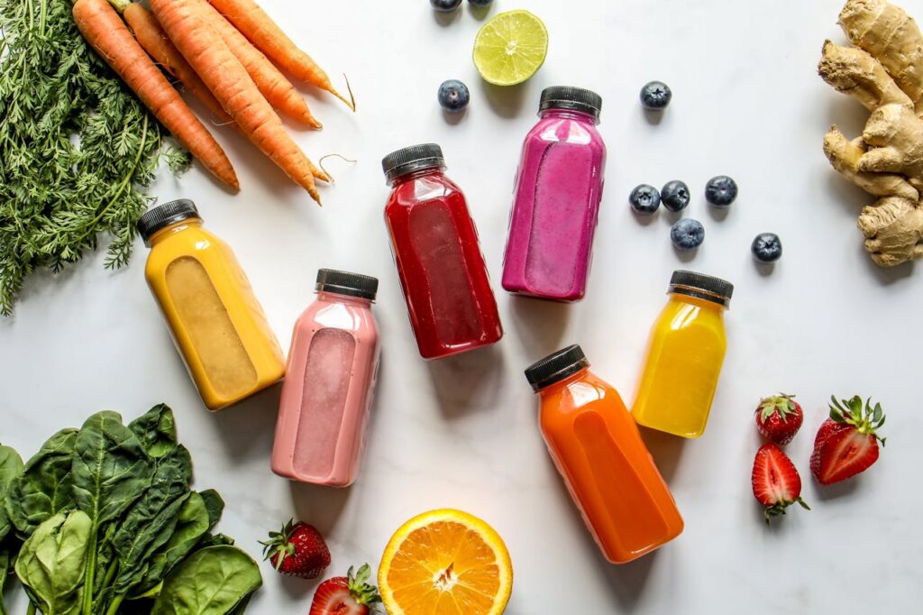 Colorful Bottles with Smoothies Beside Carrots, Ginger, Leaves and Berries
