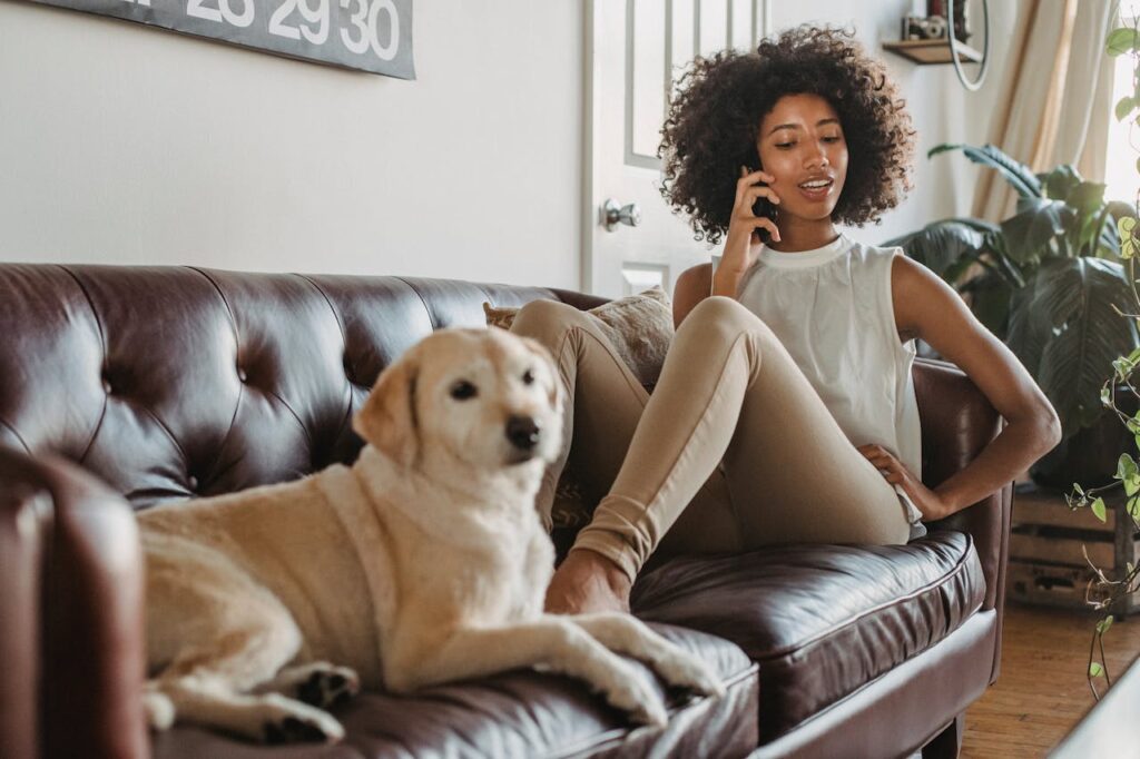 Smiling black woman talking on smartphone while lying with dog
