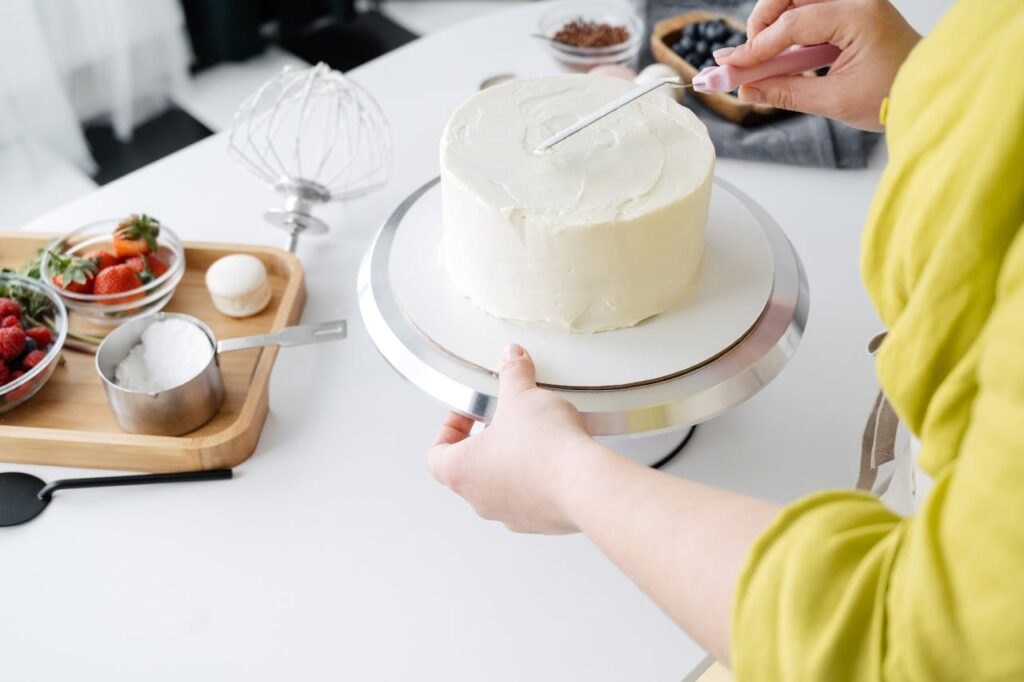 Woman hands decorating biscuit cake with cream
