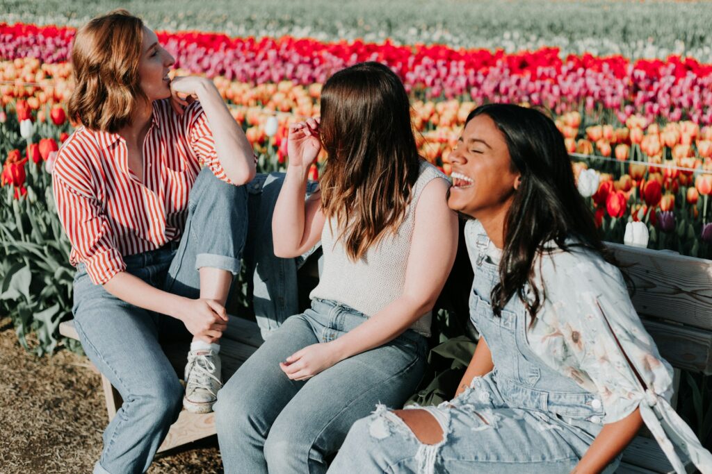 three women sitting wooden bench by the tulip flower field
