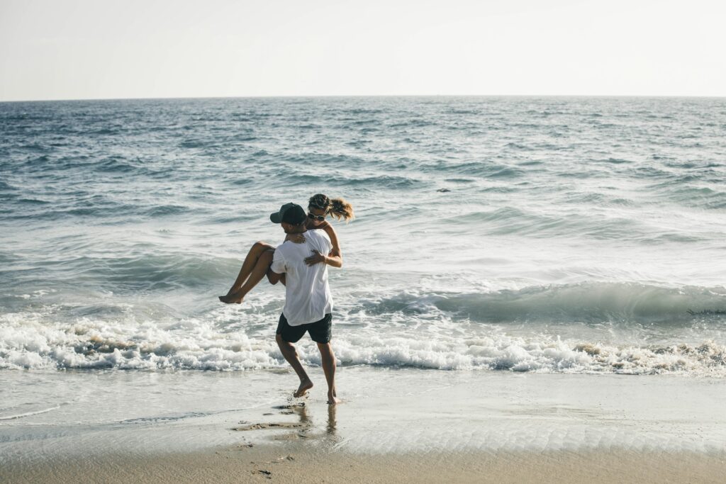man carrying woman on seashore
