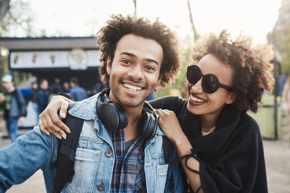 Positive and emotive young african-american people cuddling or hugging while walking in park, joking and being in good mood, wearing trendy outfit. Friendship lasts forever