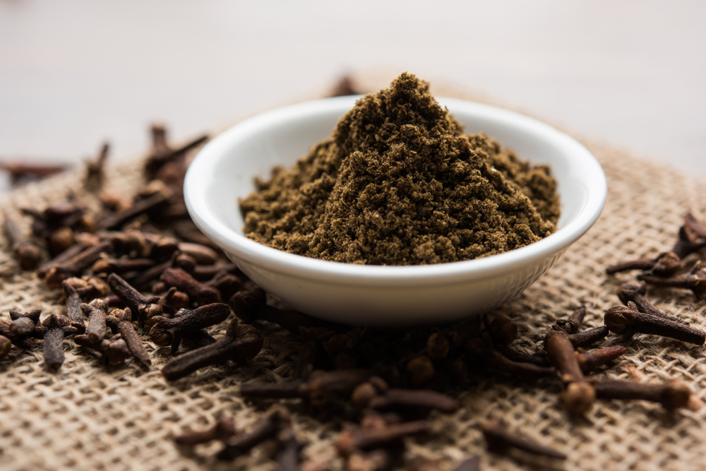 whole Cloves or laung or lavang with powder in a bowl isolated on white. Whole cloves. Selective focus