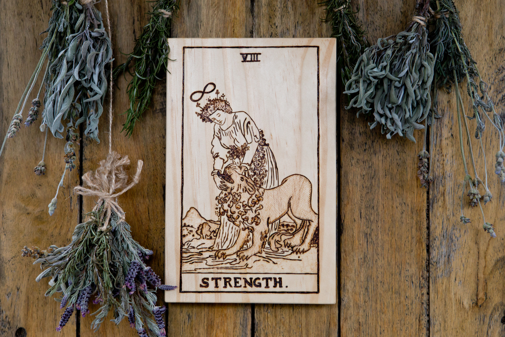 Wooden Strength card from Tarot Major Arcana with dried herbs on rustic background - hand burnt in wood by photographer