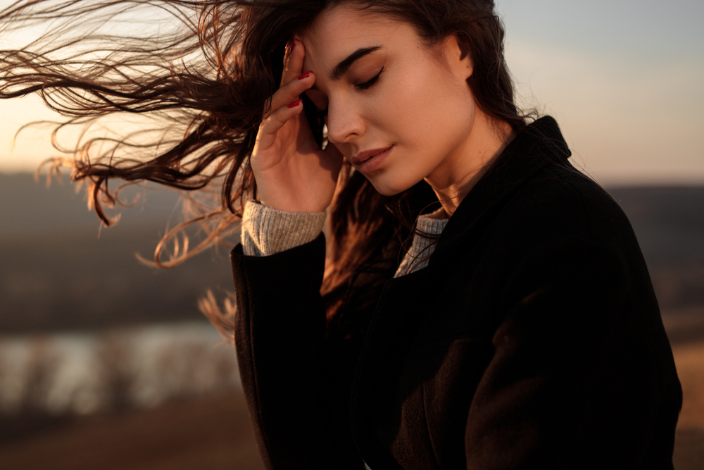Side view of exhausted lonely young female with long hair fluttering in wind having problems and thinking about life in autumn evening in nature