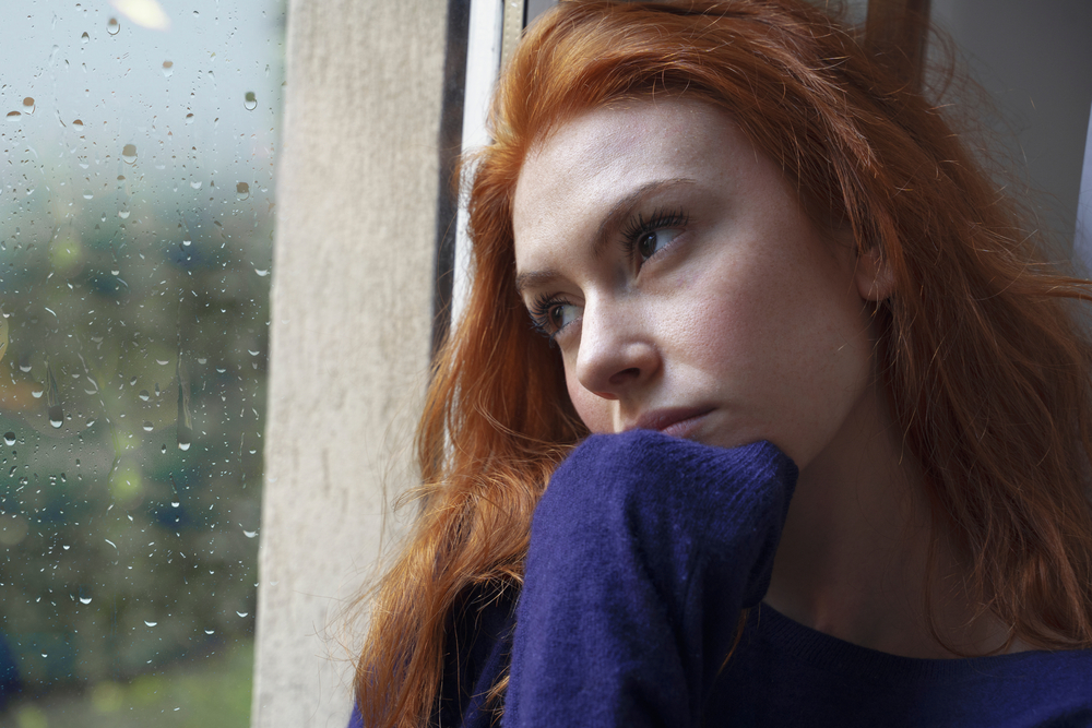 Portrait of worried girl looking through the window at home
