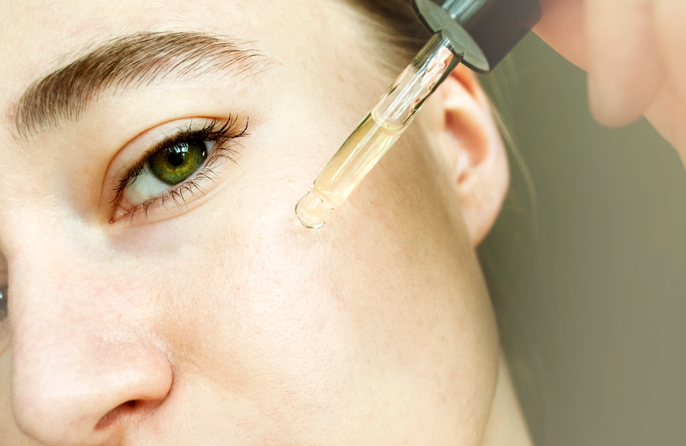Close-up portrait of woman applying glass peep liquid, skin texture. Apply a tea tree moisturizing serum to your face.