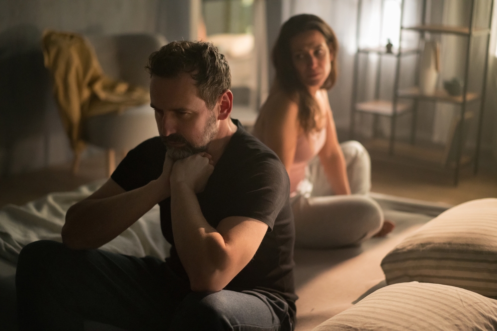 Upset mature man with his wife in bed hehind him, relationship problems concept.
