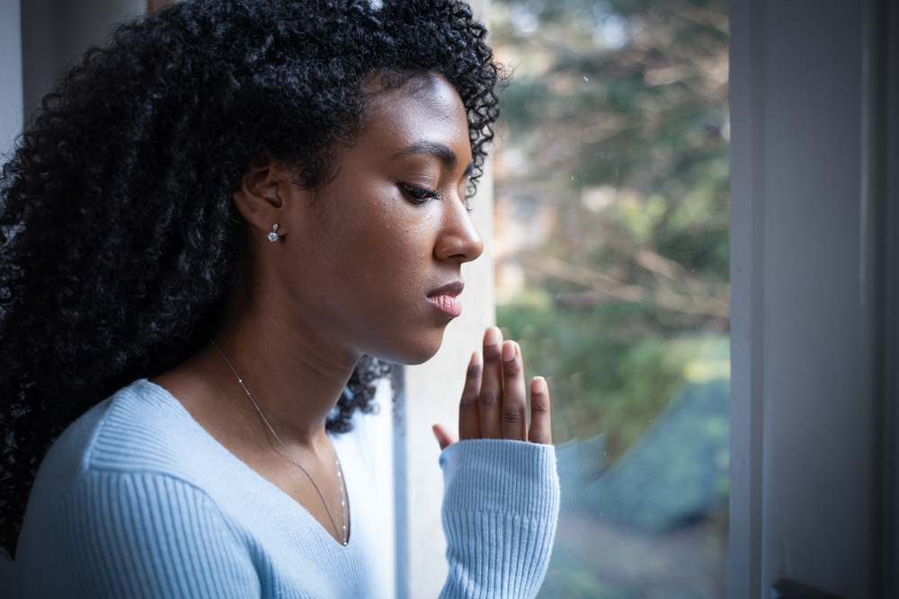 One black woman pray in front of window
