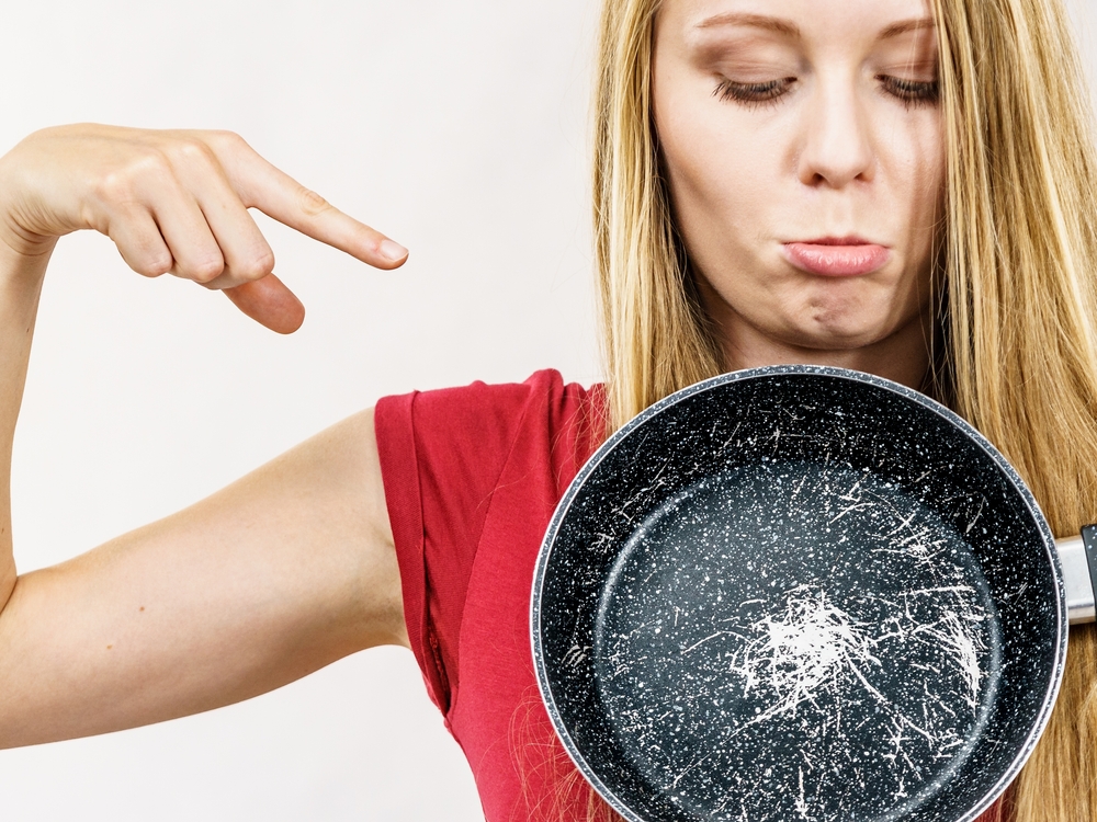 Woman holding scratched frying pan, cause of cancer. Torn coating, kitchen utensil is unusable