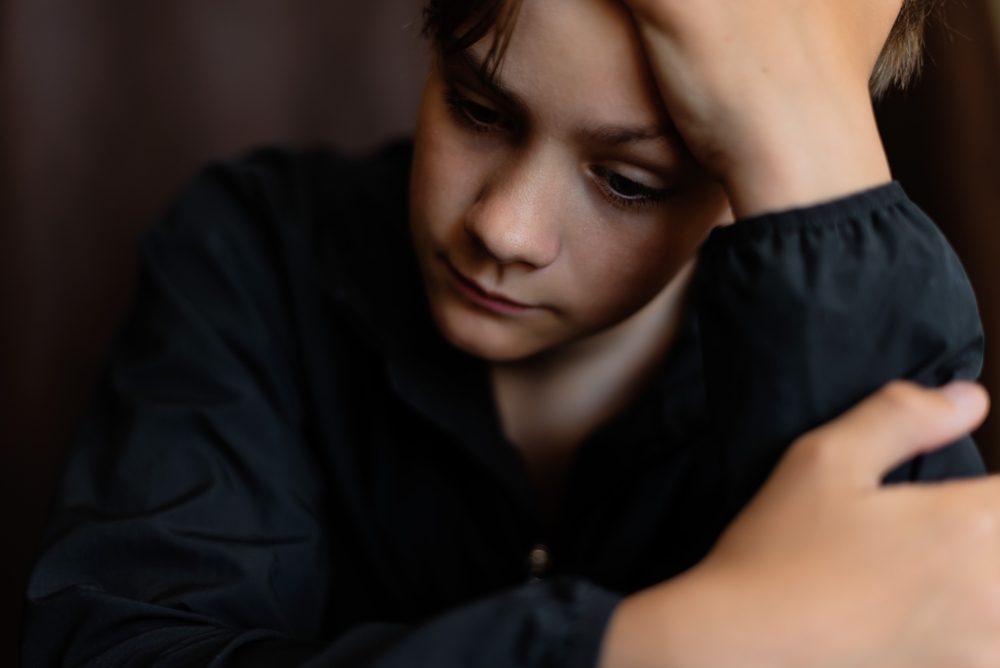 Portrait of blonde teenage boy on dark background outdoor. Low key close up shot of a young teen boy, adolescence. Selective focus. Loneliness, sadness, adolescent anxiety, emotional.