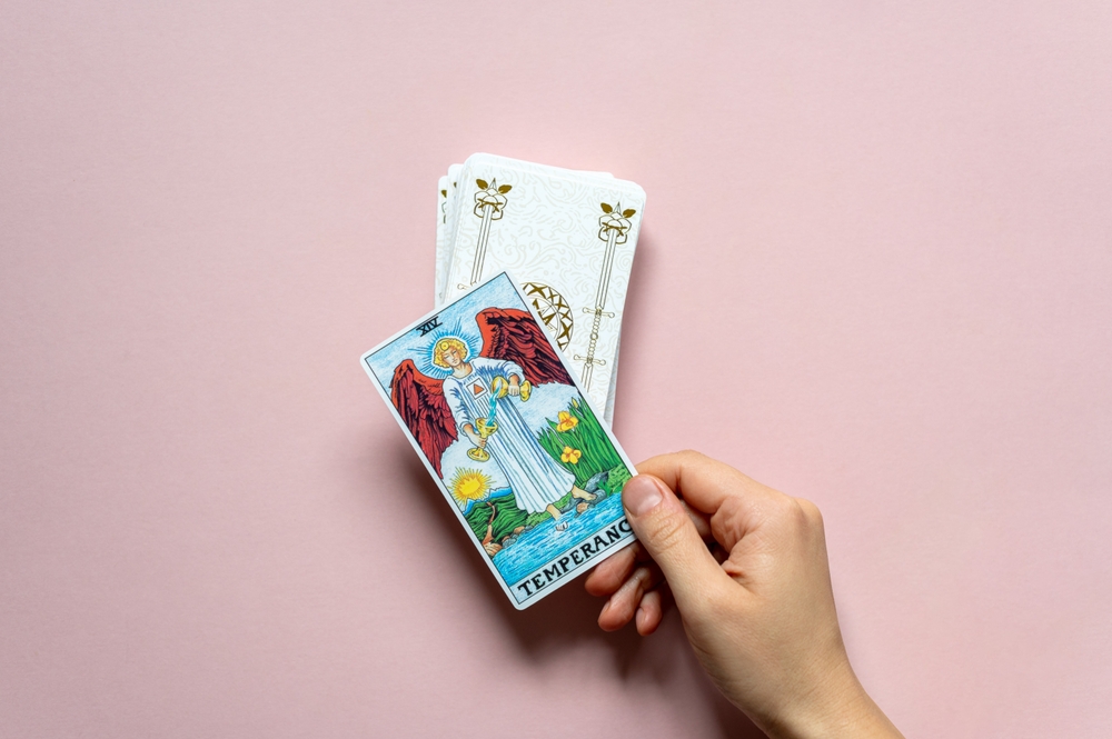 London, UK: 14 October, 2022: The 14 Major Arcana - Temperance Tarot Card of Rider Waite deck in hand on pink background