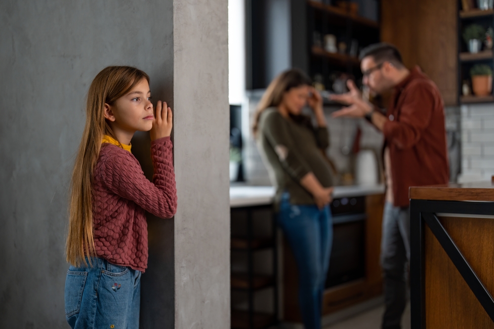 Angry man is yelling at his pregnant wife while she's holding her stomach. Parents arguing at home without knowing that their daughter is listening from a side.