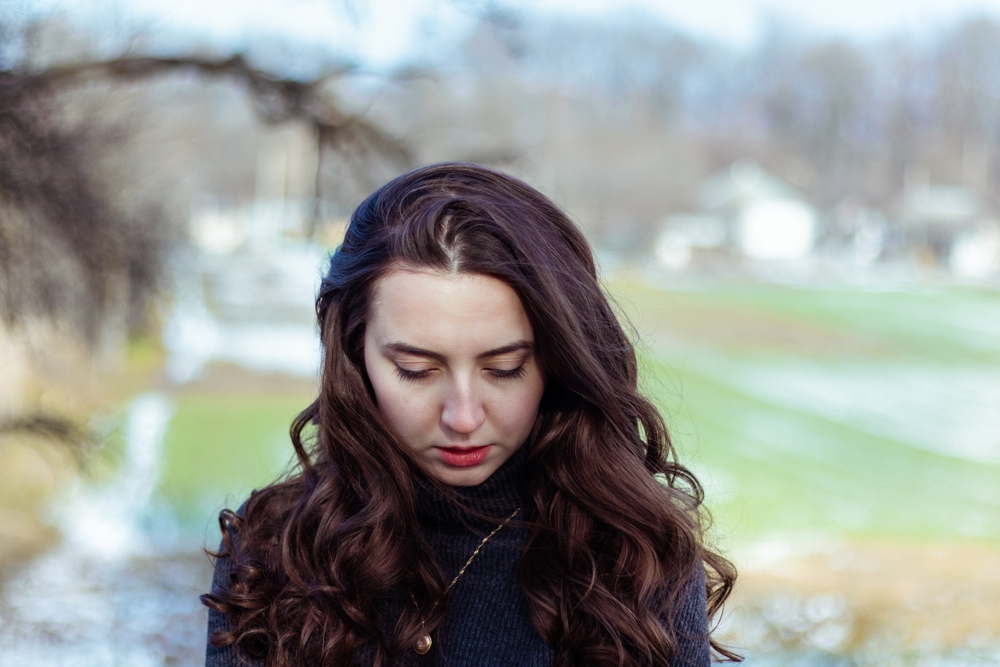 Sad woman.Girl in sadness.Portrait of a girl in nature.Beautiful curly hair.Woman looks down.Retro vintage colors.Vintage retouch.Feeling of loneliness.Winter portrait.Cold colors. Problems.Hair care.
