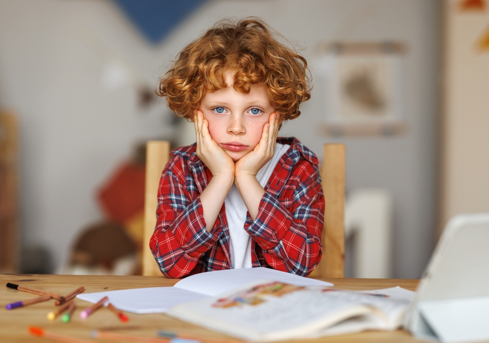 Frustrated boy thinking over difficult task and touching head while doing homework at table