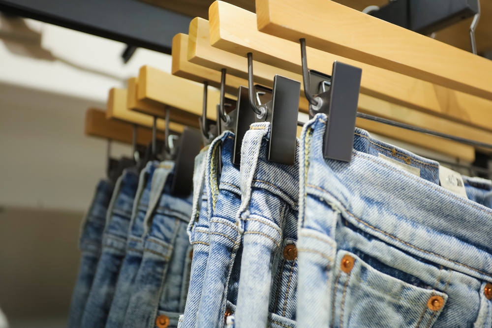 Jeans on the hanger in the store. Clothes on hangers in shop for sale. Blur background. Fashionable clothes in a boutique. Various clothing on market. Shopping in store.