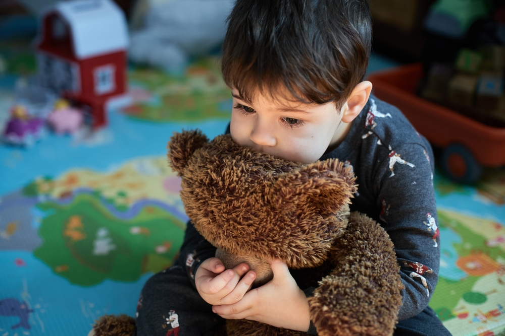 pensive baby boy hugging a toy bear in the kids room at nap time