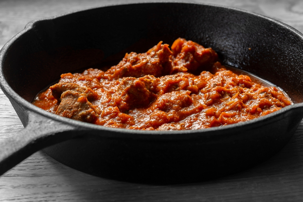 Rogan josh lamb Indian curry cooked in a cast iron frying pan. On a wooden background
