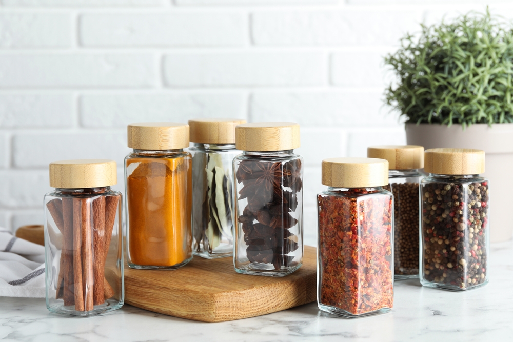 Different spices in glass jars on white marble table