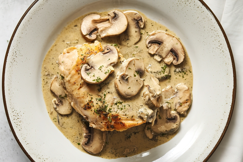 a plate with a chicken meat in cream sauce of mushrooms
